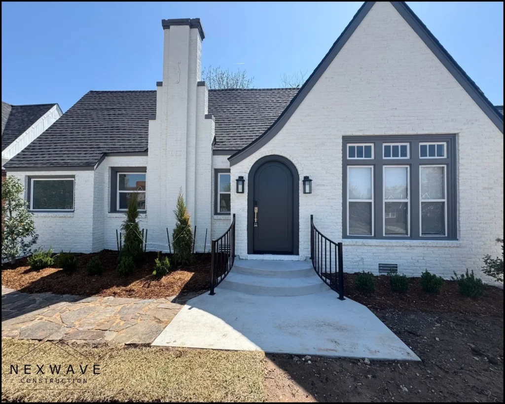 Single-story white brick house with a steep roof, arched black front door, and a concrete front porch.