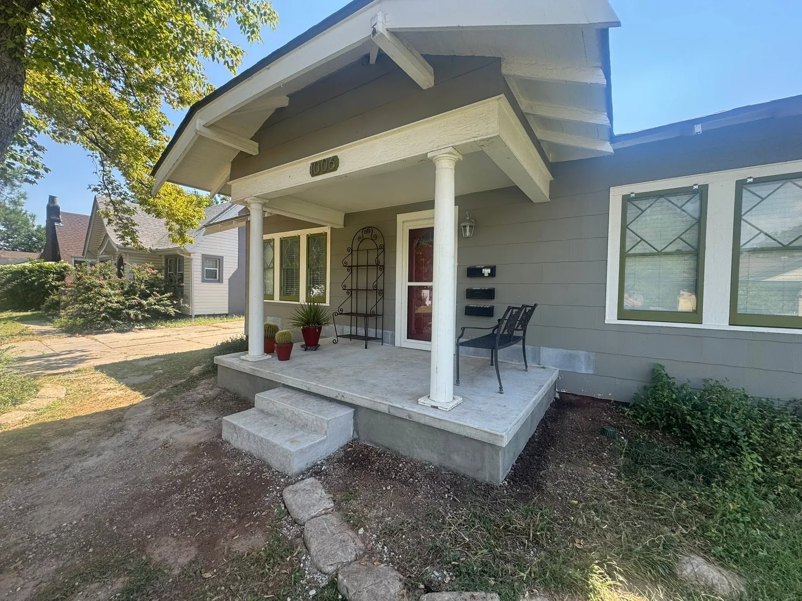 A single-story gray house with a covered front porch, two white columns, and address number 1006 above the door.