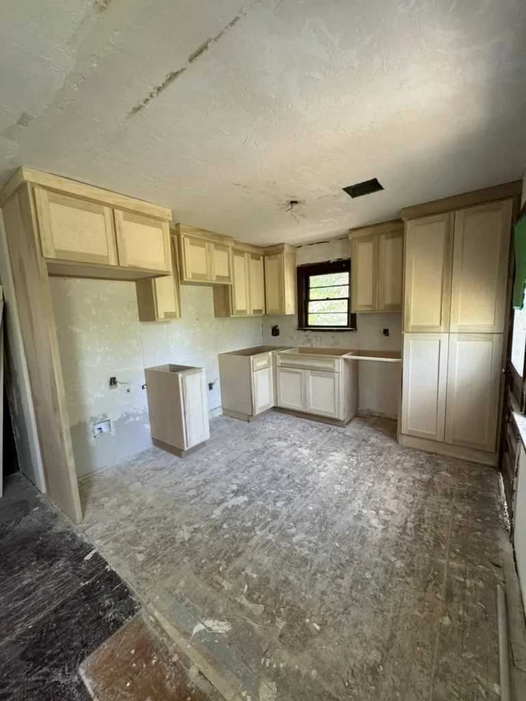 Unfinished kitchen remodel with light wood cabinets installed against bare walls and a worn subfloor.