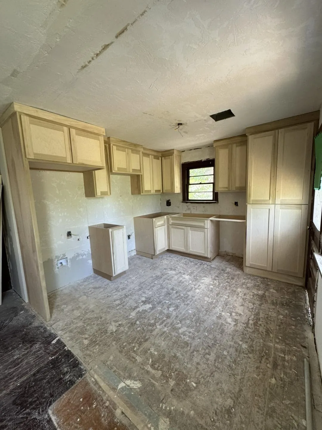 Unfinished kitchen remodel with light wood cabinets installed against bare walls and a worn subfloor.