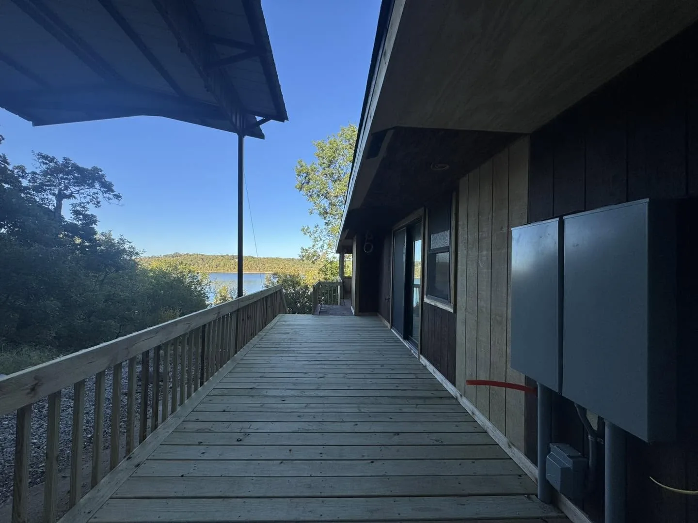 A wooden deck runs alongside a house exterior toward a view of a lake.