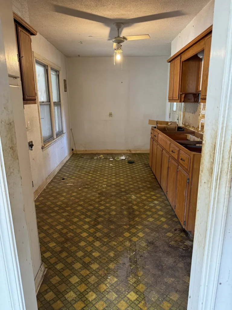 A vacant kitchen with worn checkered flooring, wooden cabinets, and a ceiling fan.