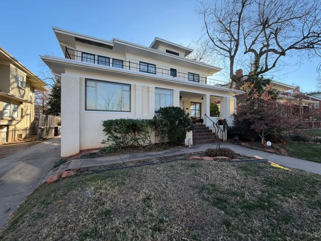 Two-story stucco house with a flat roof, a second-story balcony, and a covered front porch.