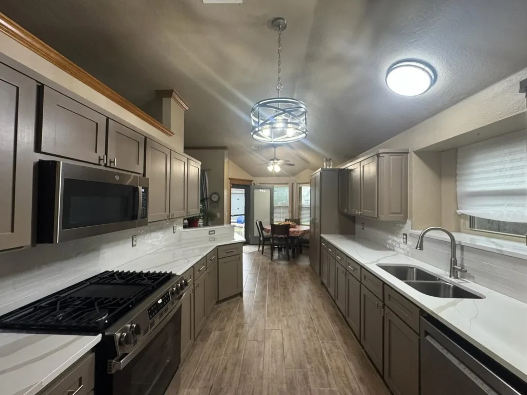 A galley kitchen with gray cabinets, white countertops, and wood-look tile flooring.