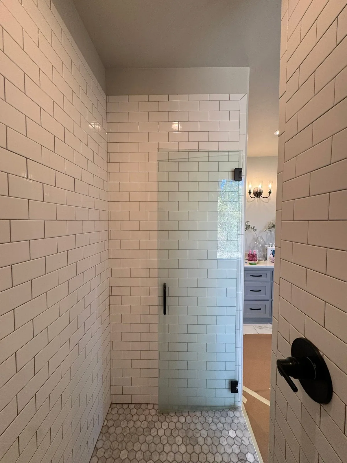 Walk-in shower with white subway tile walls, a hexagonal tile floor, and a glass door, viewed from a doorway.