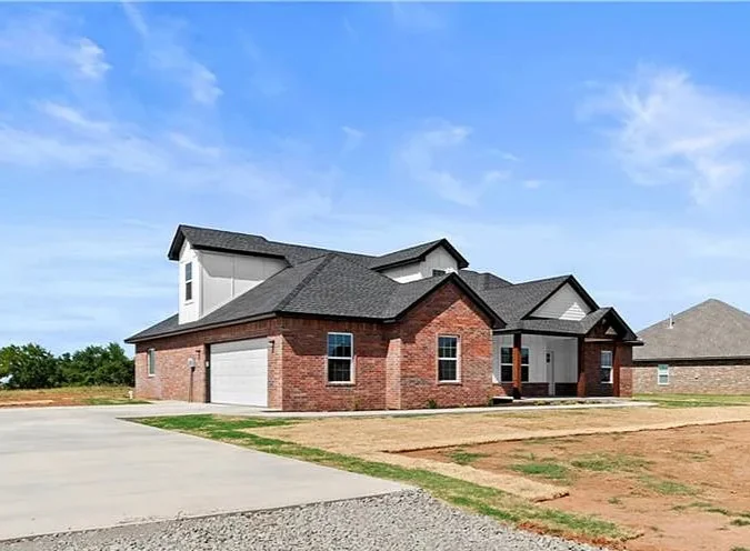 Single-story brick house with a white garage and dark shingled roof under a blue sky.