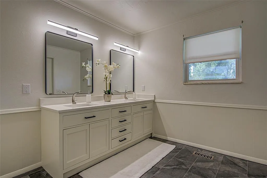 Bathroom with a white double vanity, two rectangular mirrors, wall-mounted light fixtures, and a window.