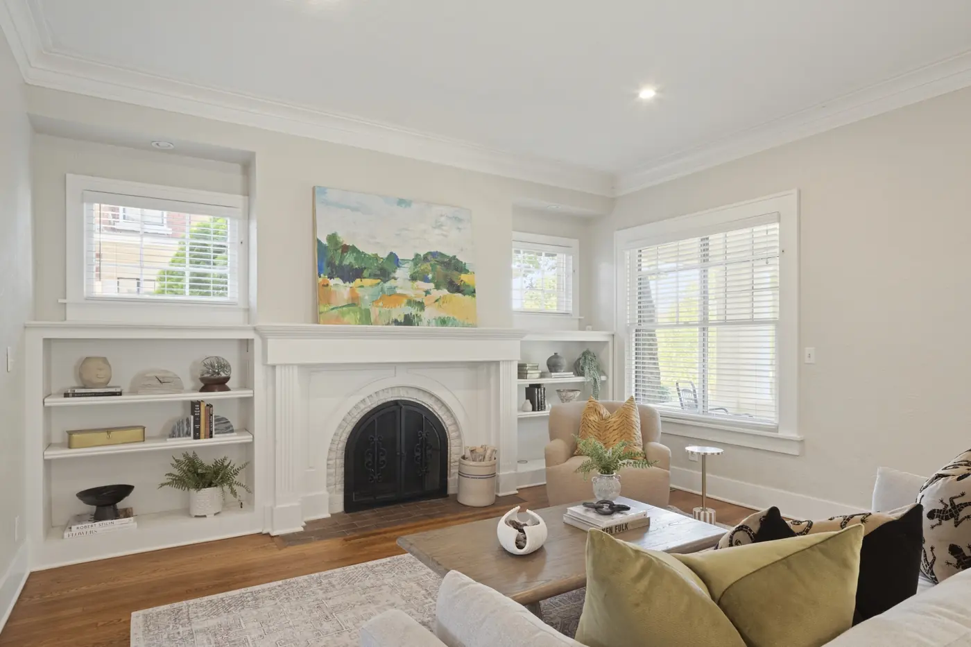 Living room with a white fireplace, landscape painting, built-in shelving, and a seating area with a coffee table.